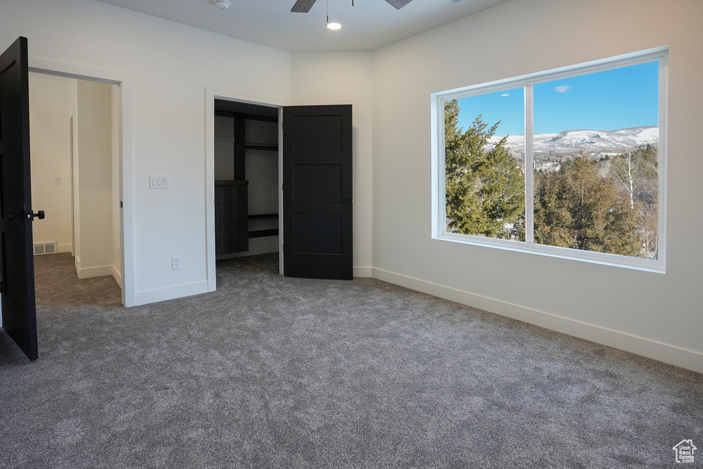Unfurnished bedroom with dark colored carpet, a mountain view, and ceiling fan