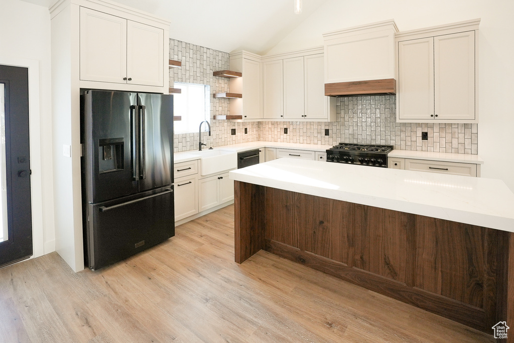 Kitchen featuring lofted ceiling, sink, light hardwood / wood-style flooring, backsplash, and black appliances