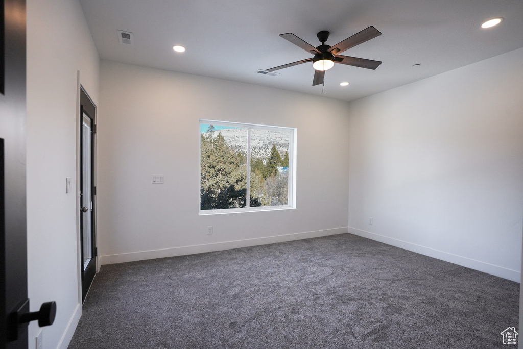 Spare room with ceiling fan and dark colored carpet