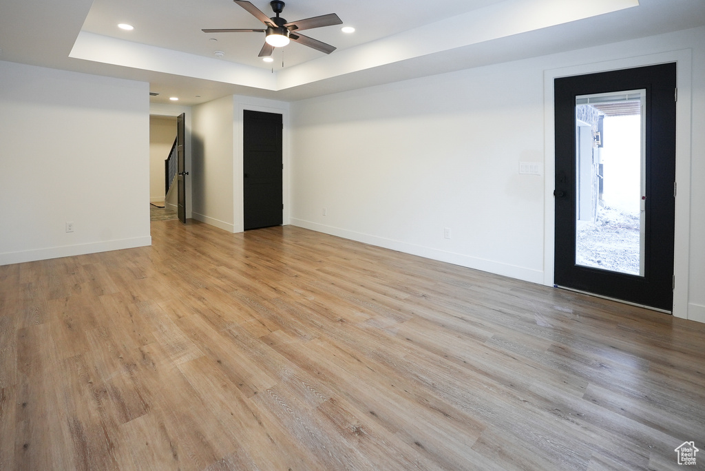 Empty room featuring a tray ceiling, ceiling fan, and light wood-type flooring