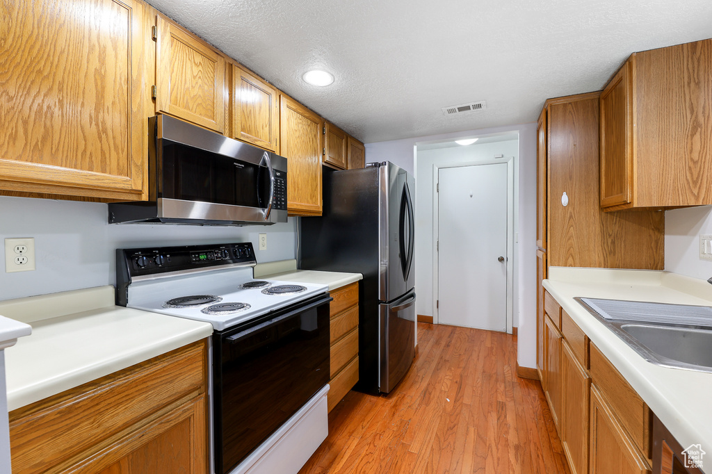 Kitchen with a textured ceiling, appliances with stainless steel finishes, sink, and light hardwood / wood-style floors