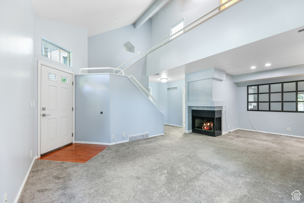 Unfurnished living room with a fireplace, a towering ceiling, and carpet flooring