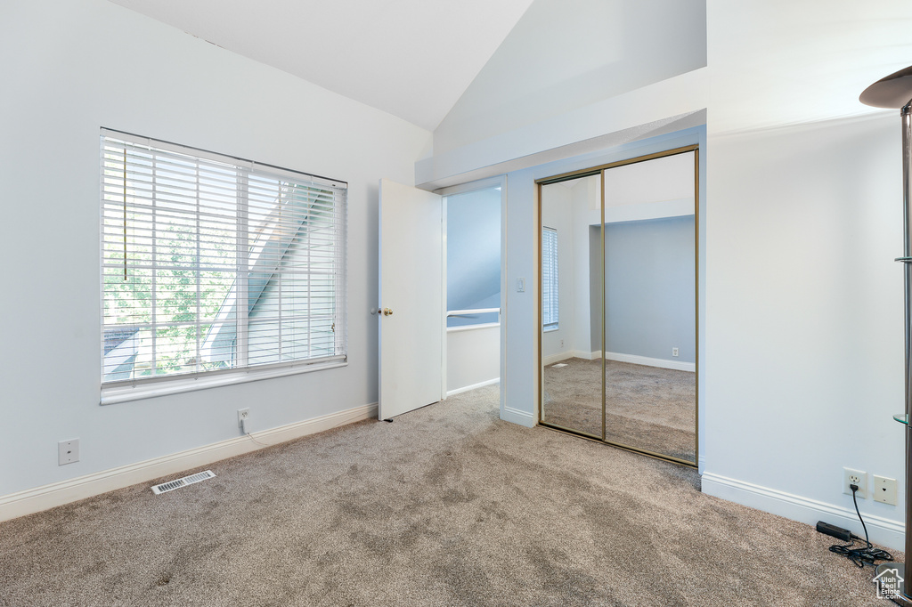 Unfurnished bedroom with vaulted ceiling, light colored carpet, and a closet