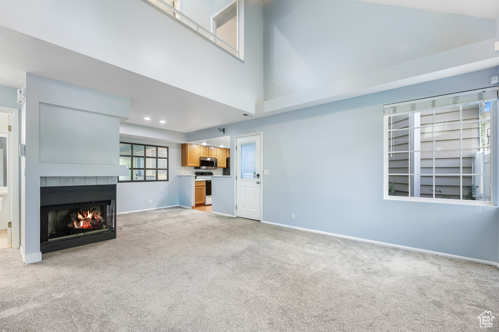 Unfurnished living room with a towering ceiling, a tiled fireplace, and light colored carpet