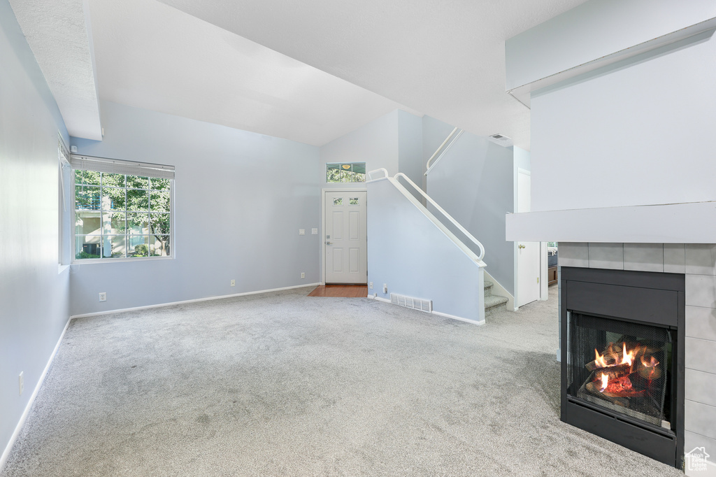 Unfurnished living room featuring light colored carpet, lofted ceiling, and a tile fireplace