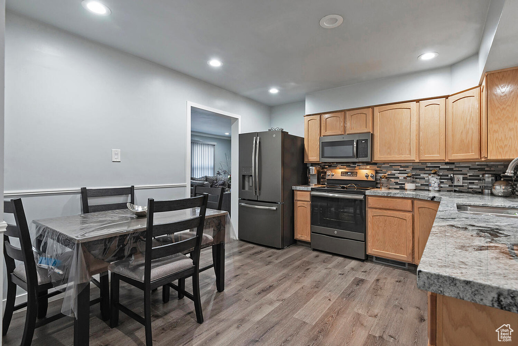 Kitchen with sink, appliances with stainless steel finishes, light hardwood / wood-style floors, and tasteful backsplash