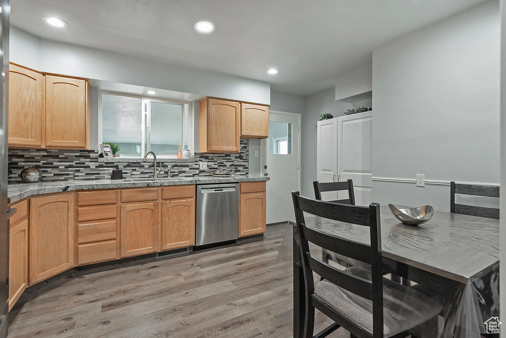 Kitchen with light brown cabinets, sink, stainless steel dishwasher, light hardwood / wood-style floors, and decorative backsplash