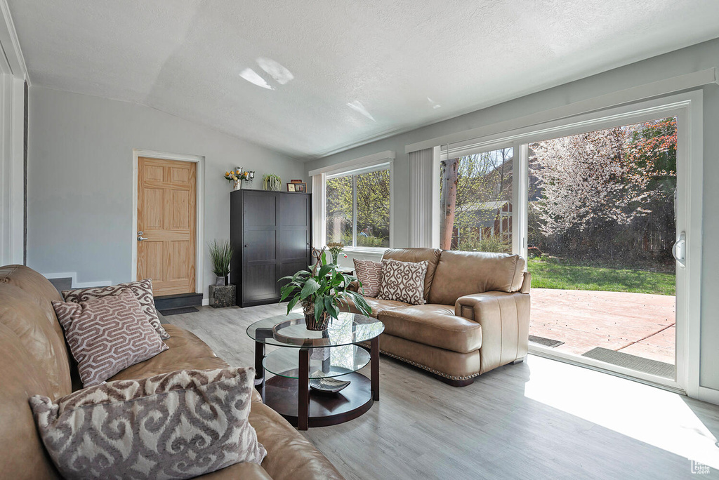 Living room with vaulted ceiling, a textured ceiling, and light hardwood / wood-style floors