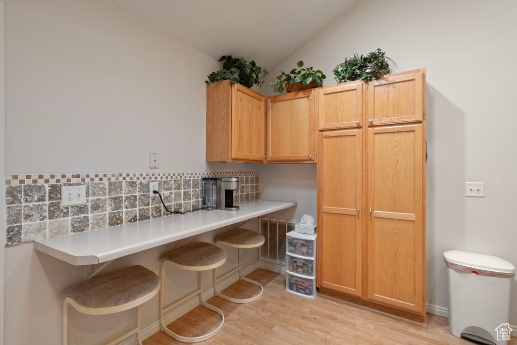Kitchen with a breakfast bar, light wood-type flooring, lofted ceiling, decorative backsplash, and light brown cabinetry