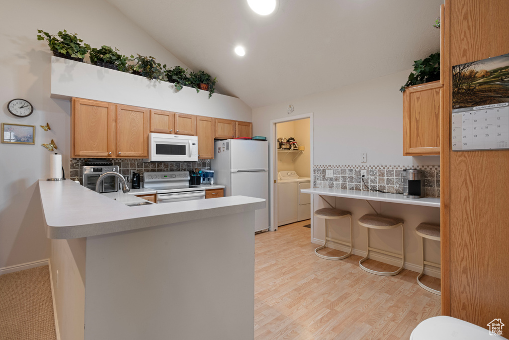 Kitchen featuring a kitchen breakfast bar, independent washer and dryer, white appliances, kitchen peninsula, and sink