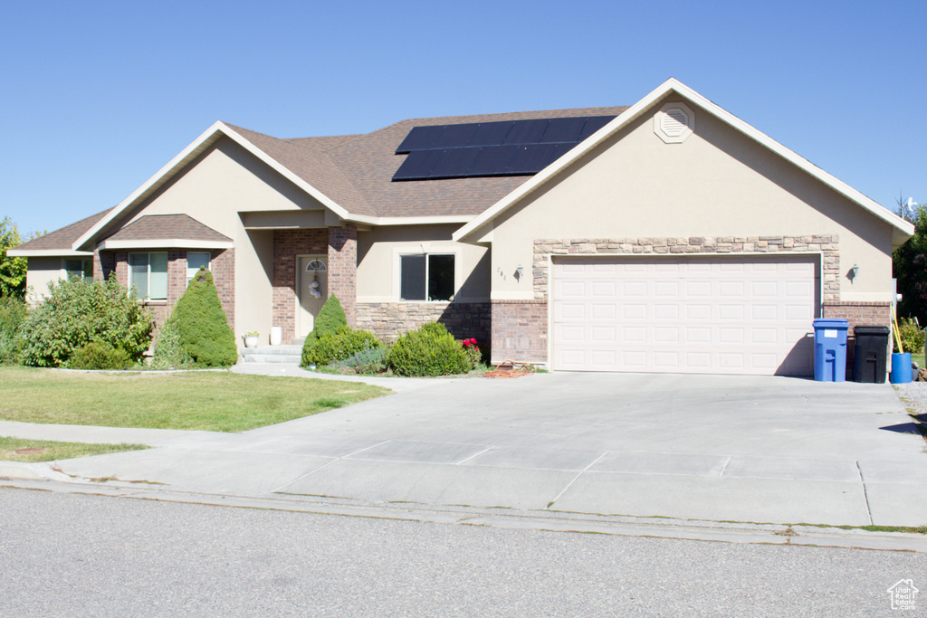 View of front facade featuring a front lawn, solar panels, and a garage