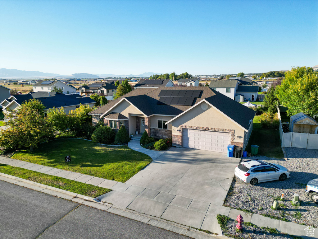 View of front facade with a mountain view, a garage, solar panels, and a front lawn