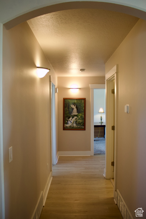 Corridor with a textured ceiling and light hardwood / wood-style floors