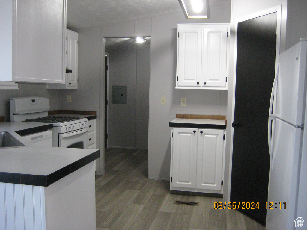 Kitchen featuring white cabinets, white appliances, wood-type flooring, and a textured ceiling