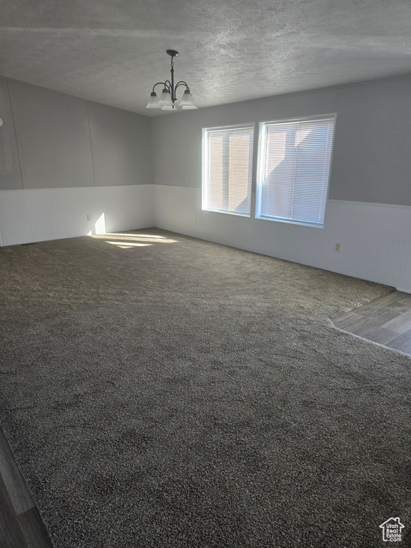 Carpeted spare room with vaulted ceiling, a textured ceiling, and a chandelier