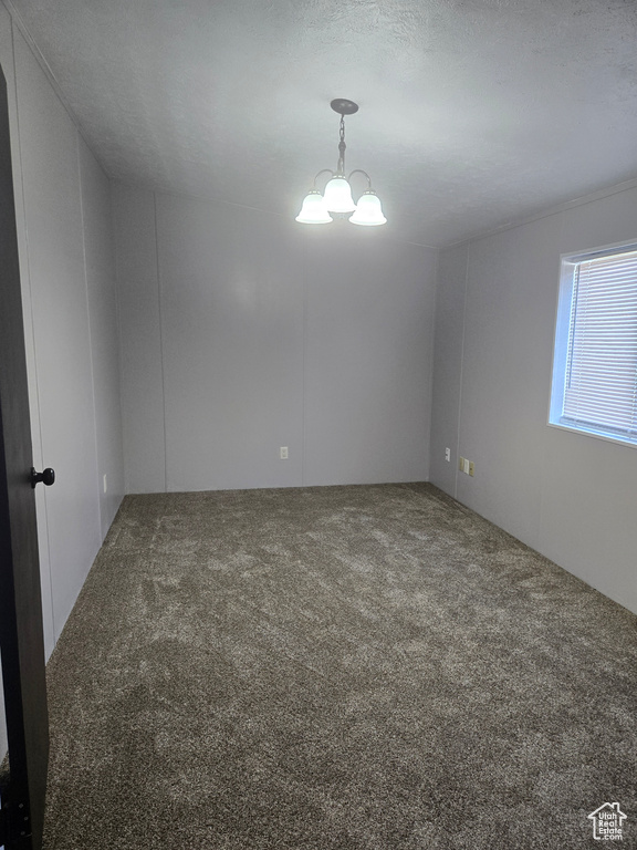 Unfurnished room with a textured ceiling, carpet flooring, and an inviting chandelier