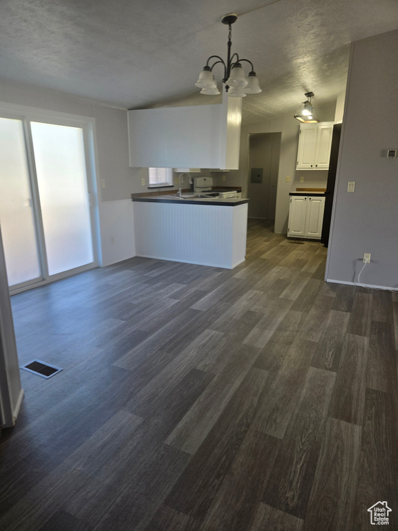 Kitchen featuring dark hardwood / wood-style floors, white cabinetry, kitchen peninsula, an inviting chandelier, and decorative light fixtures