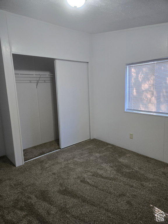 Unfurnished bedroom with a textured ceiling, dark colored carpet, and a closet