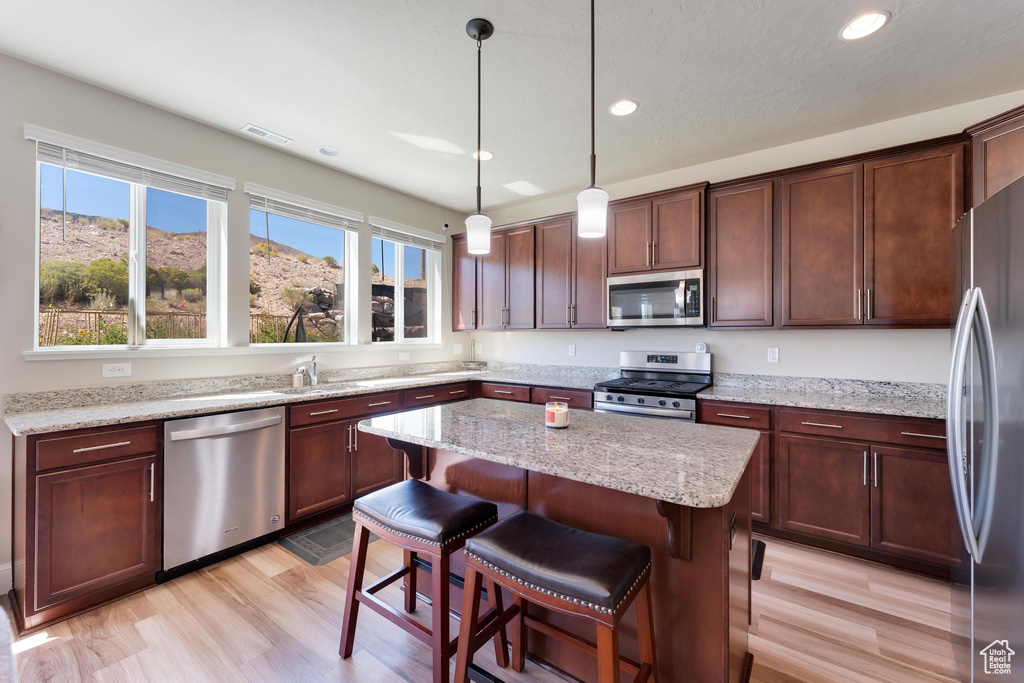 Kitchen with light stone counters, light hardwood / wood-style floors, a kitchen island, stainless steel appliances, and decorative light fixtures