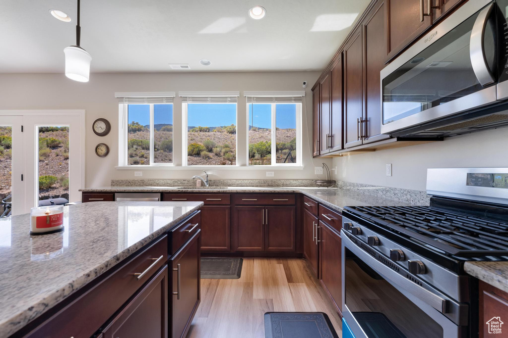 Kitchen featuring light wood-type flooring, sink, decorative light fixtures, stainless steel appliances, and light stone countertops