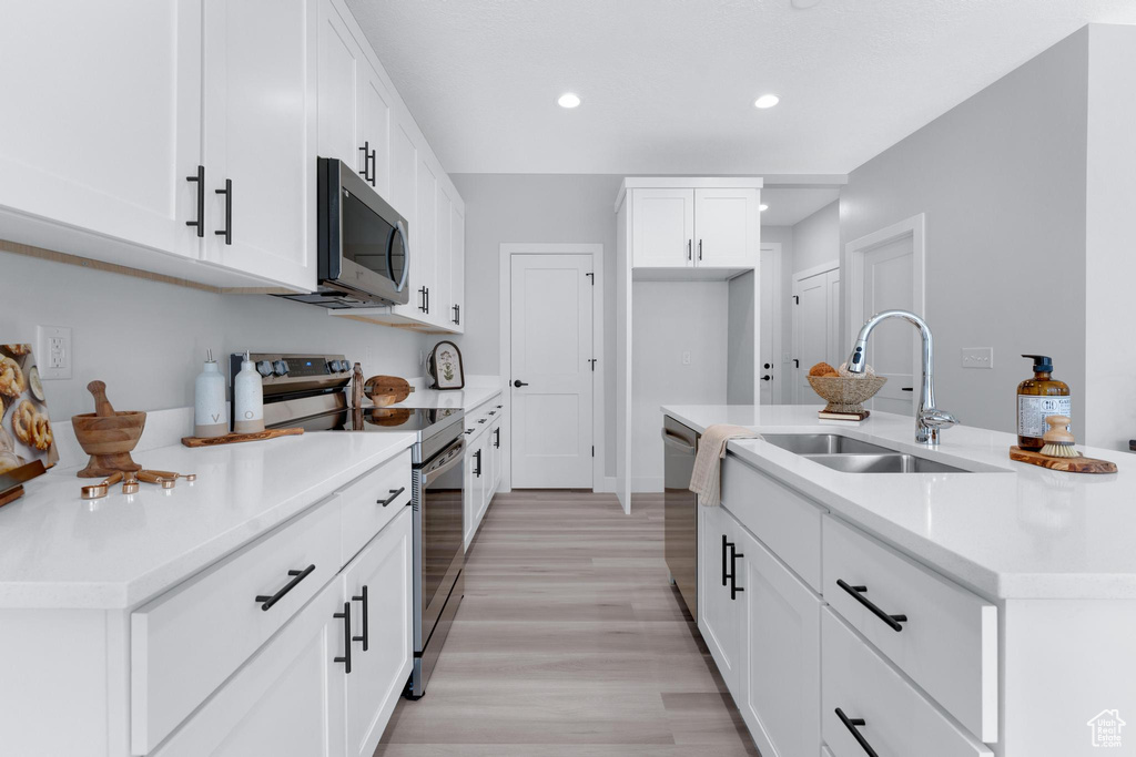 Kitchen featuring light wood-type flooring, sink, white cabinets, a center island with sink, and appliances with stainless steel finishes