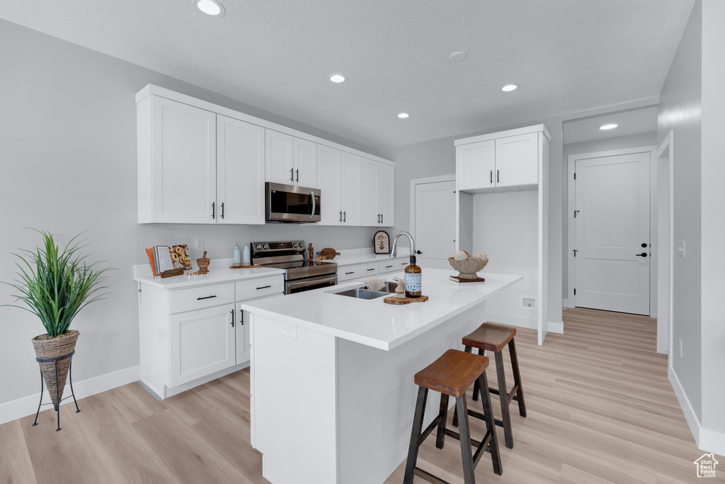 Kitchen featuring sink, light hardwood / wood-style flooring, a center island with sink, white cabinetry, and stainless steel appliances