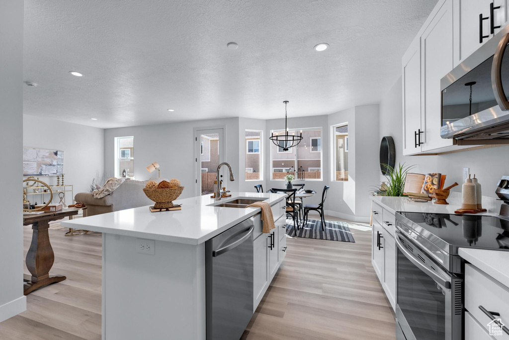 Kitchen with white cabinets, light hardwood / wood-style floors, a center island with sink, and appliances with stainless steel finishes