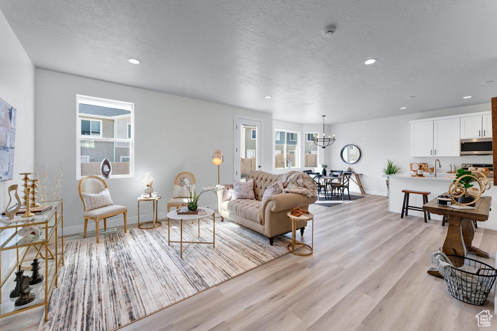 Living room with an inviting chandelier, a textured ceiling, light wood-type flooring, and sink