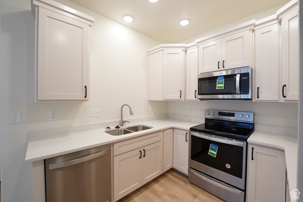 Kitchen featuring white cabinets, light hardwood / wood-style floors, appliances with stainless steel finishes, and sink