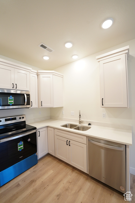 Kitchen with stainless steel appliances, white cabinetry, light wood-type flooring, and sink