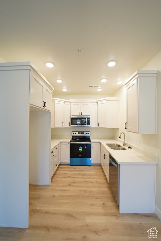 Kitchen featuring white cabinets, sink, appliances with stainless steel finishes, and light hardwood / wood-style floors