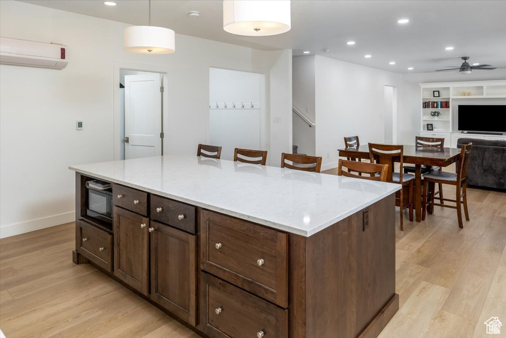 Kitchen featuring pendant lighting, light hardwood / wood-style floors, a kitchen island, built in microwave, and ceiling fan