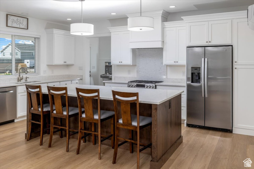 Kitchen featuring white cabinets, a center island, appliances with stainless steel finishes, and decorative light fixtures