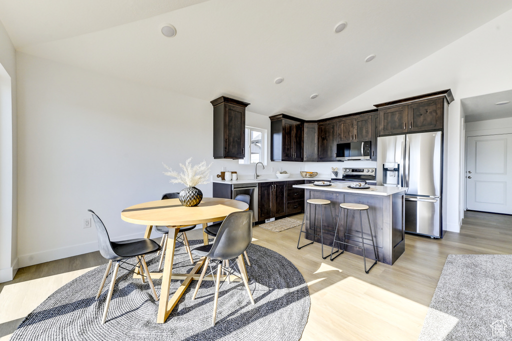 Kitchen featuring dark brown cabinets, light hardwood / wood-style floors, a center island, vaulted ceiling, and stainless steel appliances