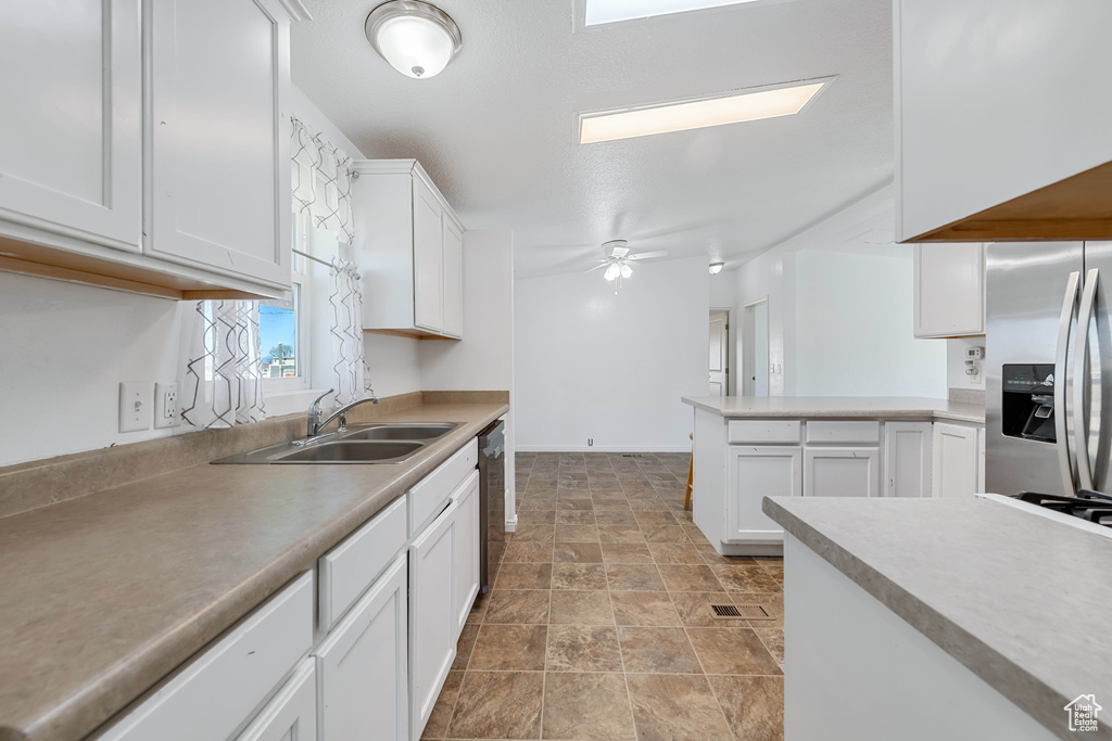 Kitchen with stainless steel fridge, white cabinetry, black dishwasher, ceiling fan, and sink