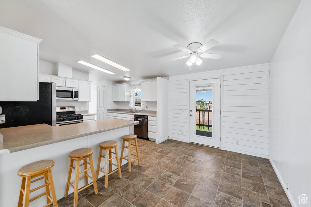 Kitchen featuring appliances with stainless steel finishes, white cabinetry, a breakfast bar, kitchen peninsula, and ceiling fan