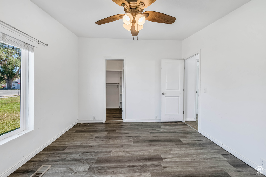 Unfurnished bedroom featuring a closet, ceiling fan, a walk in closet, and dark wood-type flooring