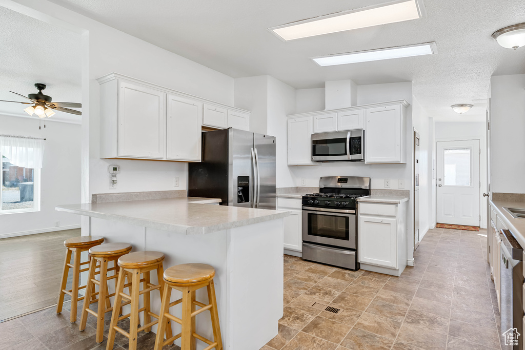 Kitchen featuring a kitchen breakfast bar, white cabinets, kitchen peninsula, stainless steel appliances, and ceiling fan