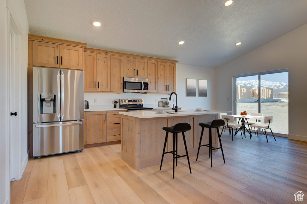 Kitchen featuring a center island with sink, appliances with stainless steel finishes, light wood-type flooring, and vaulted ceiling