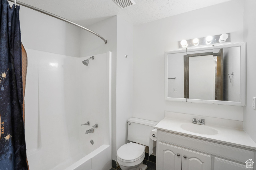 Full bathroom with vanity, shower / bath combo with shower curtain, toilet, and a textured ceiling