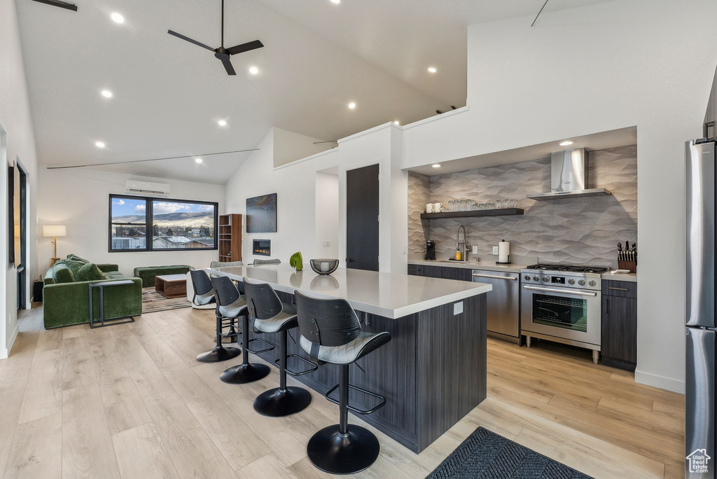 Kitchen featuring a kitchen breakfast bar, wall chimney exhaust hood, stainless steel appliances, and light hardwood / wood-style floors