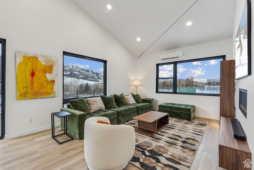 Living room with light hardwood / wood-style flooring, high vaulted ceiling, and a wall mounted air conditioner