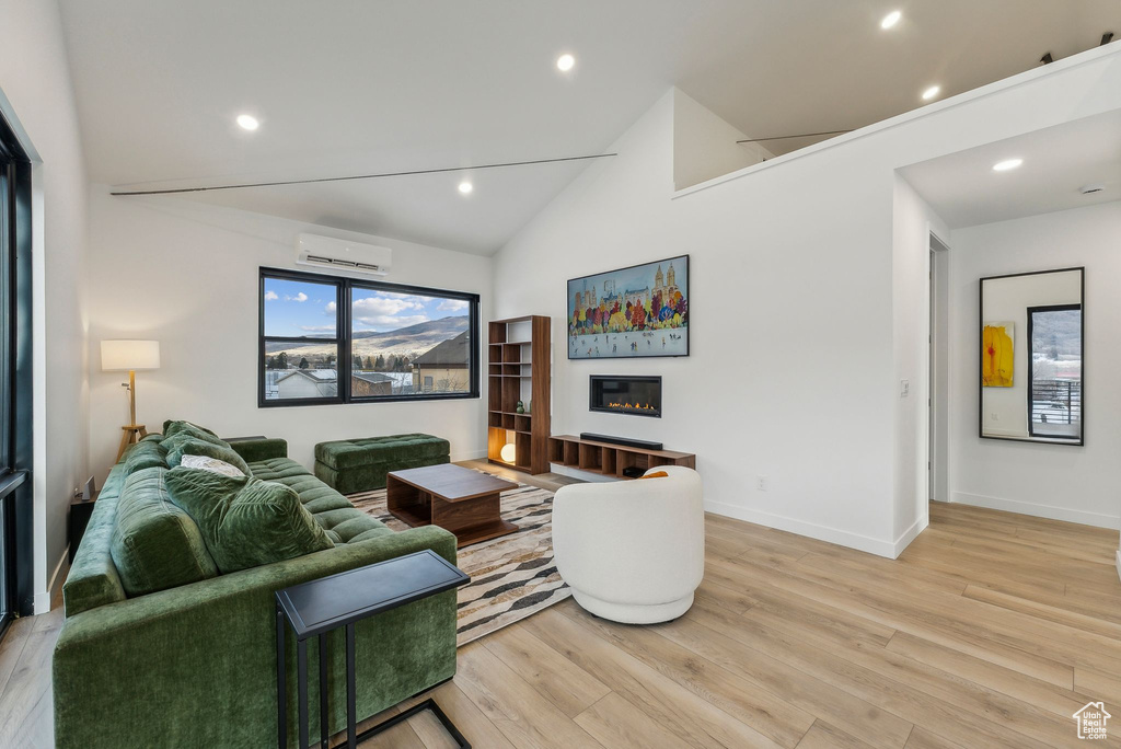 Living room featuring an AC wall unit, high vaulted ceiling, and light hardwood / wood-style flooring