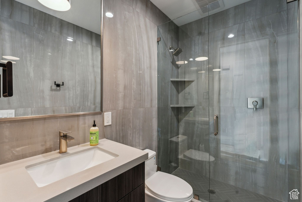 Bathroom with vanity, toilet, a shower with door, and tile walls