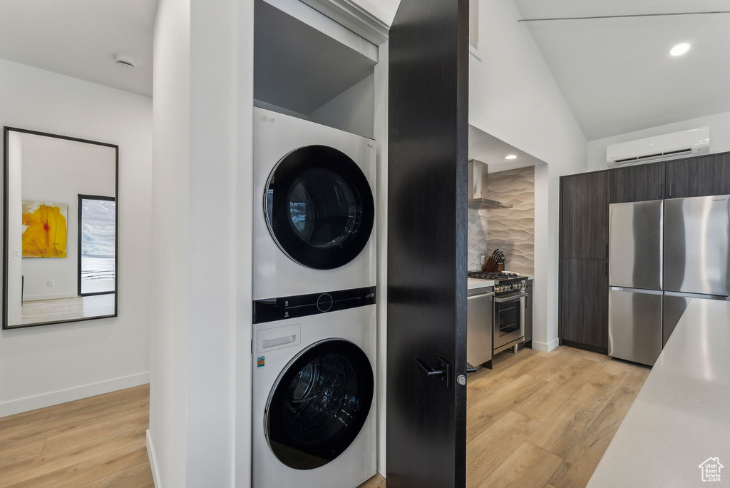 Laundry room featuring light hardwood / wood-style floors, a wall unit AC, and stacked washer and clothes dryer