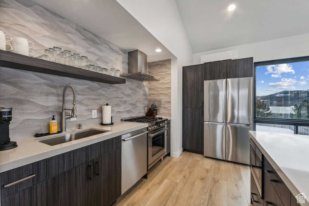 Kitchen featuring sink, wall chimney range hood, tasteful backsplash, light hardwood / wood-style floors, and appliances with stainless steel finishes