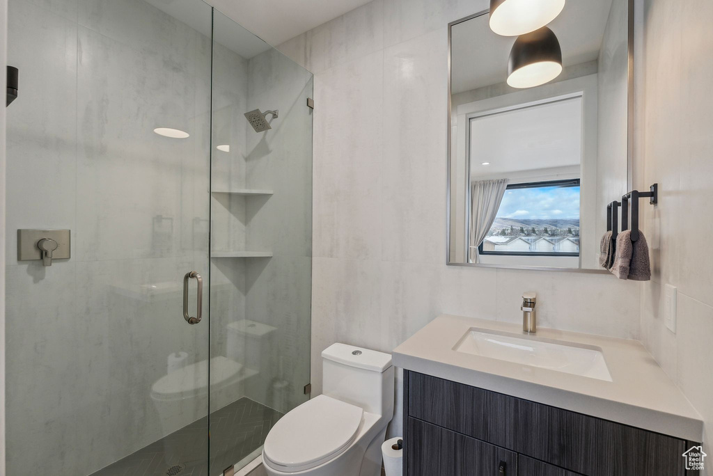 Bathroom featuring a shower with door, vanity, tile walls, and toilet