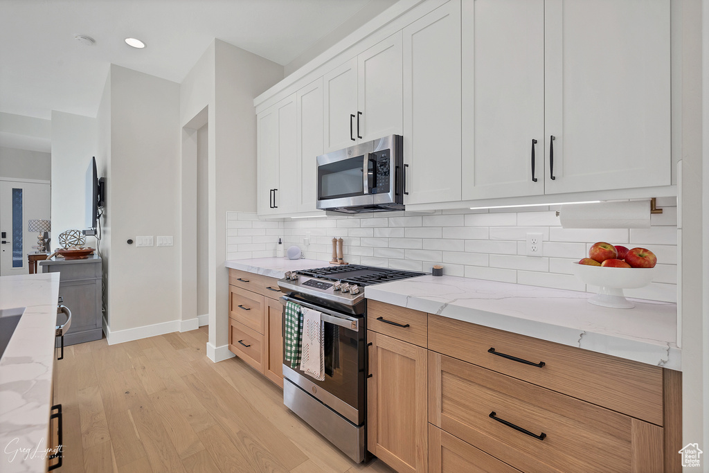 Kitchen featuring appliances with stainless steel finishes, white cabinetry, light stone counters, backsplash, and light wood-type flooring