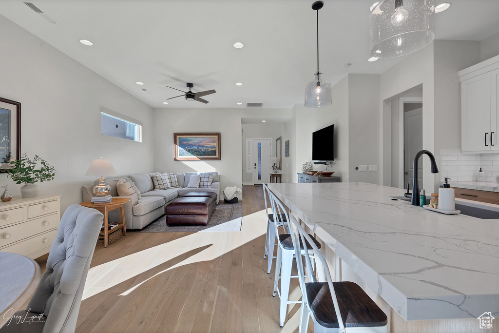 Kitchen with pendant lighting, light stone countertops, tasteful backsplash, white cabinetry, and light wood-type flooring