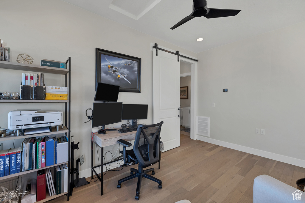 Office area featuring a barn door, light wood-type flooring, and ceiling fan